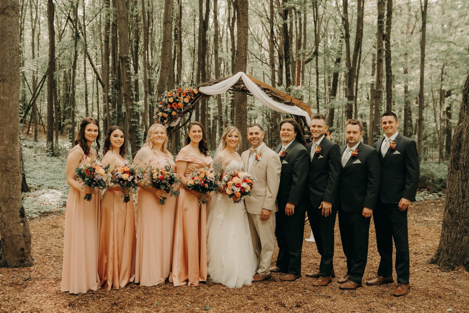 Wedding party with bride, groom, bridesmaids in blush and groomsmen in black, in a forest ceremony setting