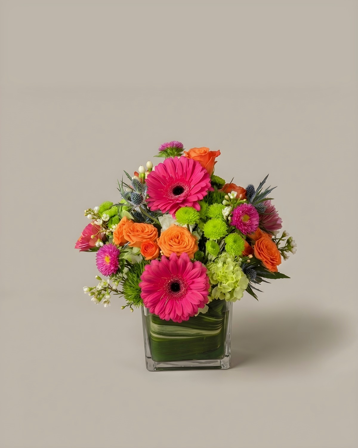 Hot pink gerbera and green mums in a leaf-lined cube vase