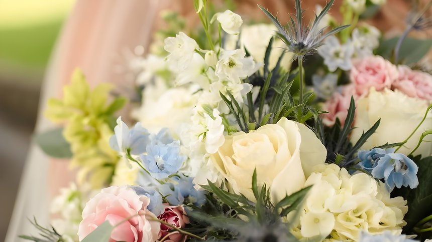 A bridal bouquet with cream roses, blue delphinium, pink carnations and sea holly