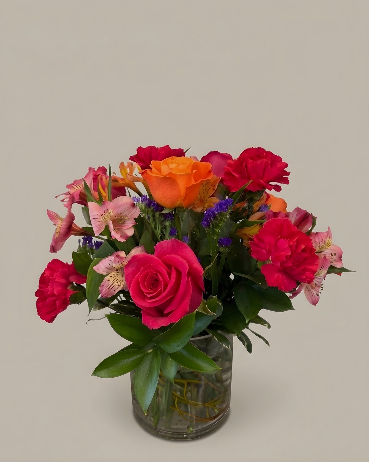 Hot pink roses, orange gerberas and red carnations in a clear glass vase