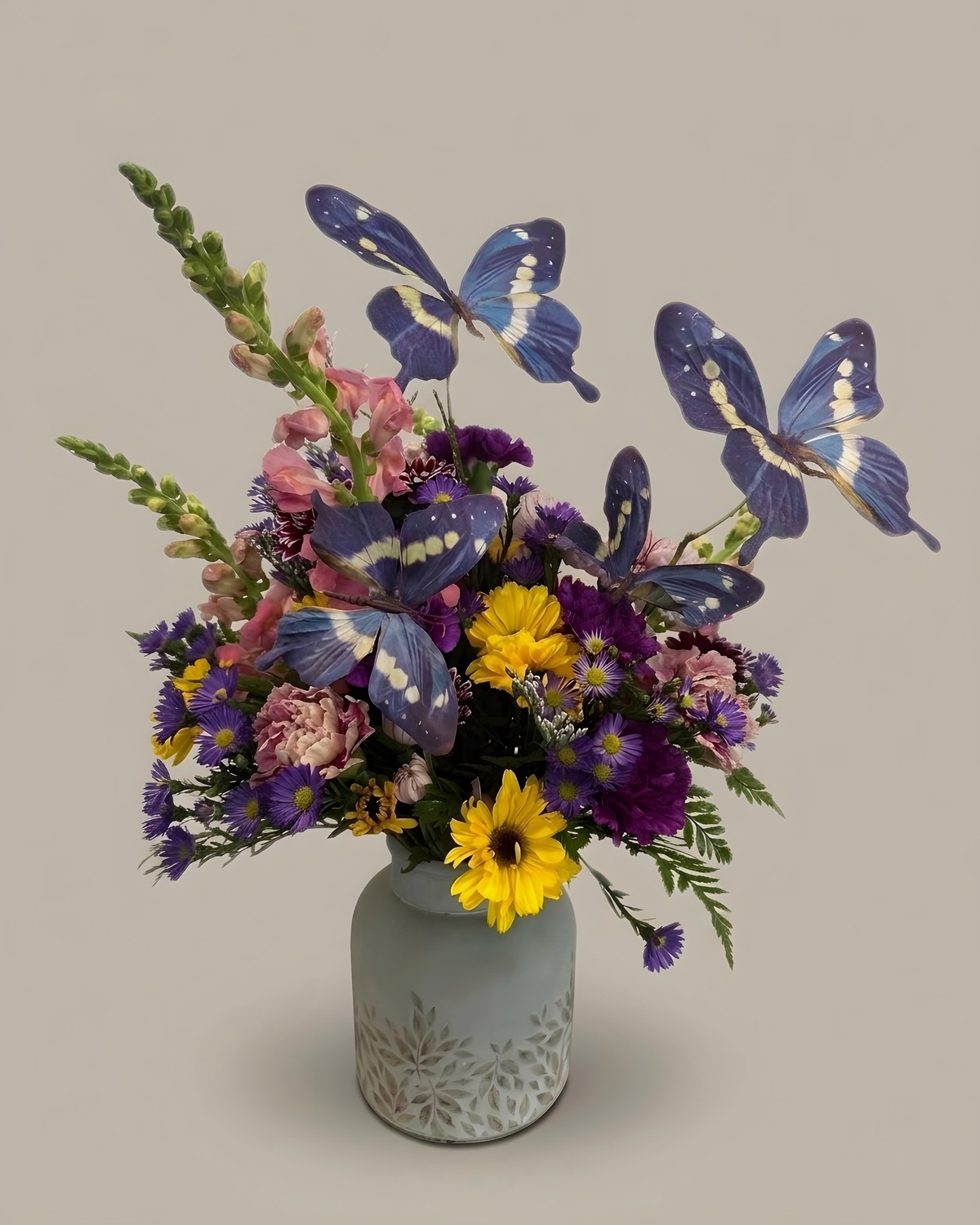 Purple asters and yellow daisies with blue butterfly picks in a grey vase