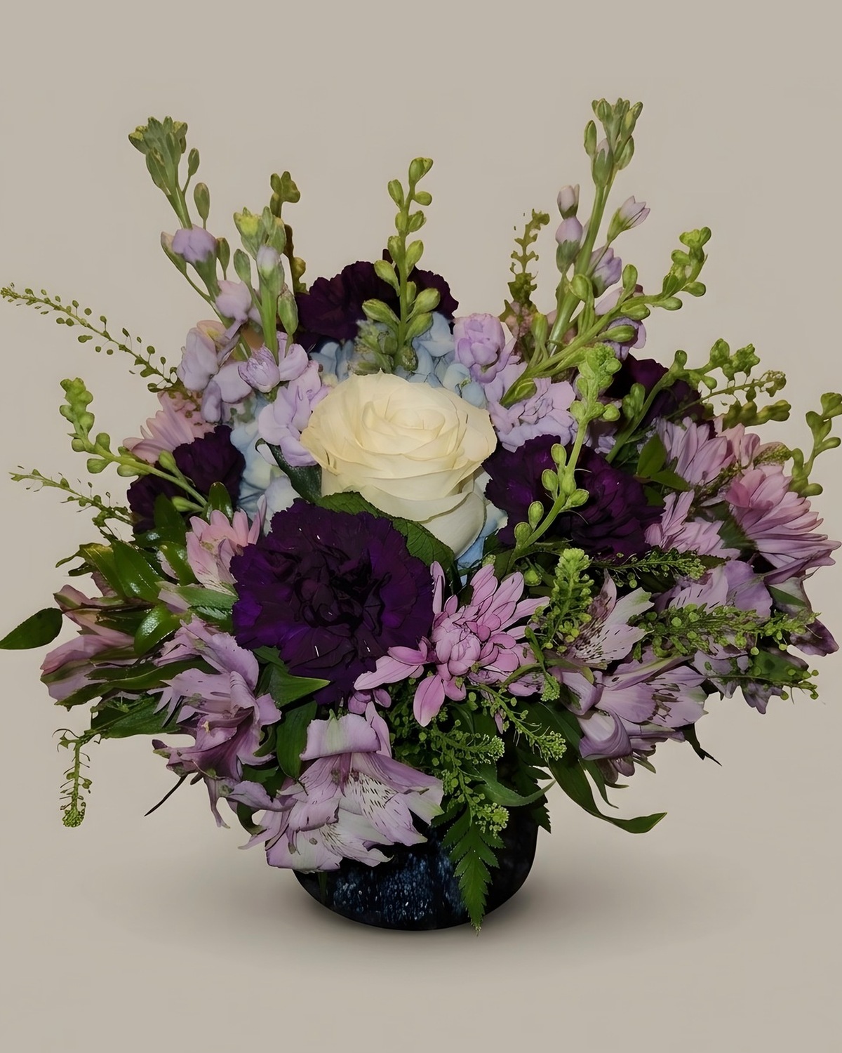 A white rose with lavender asters and purple blooms in a dark vase